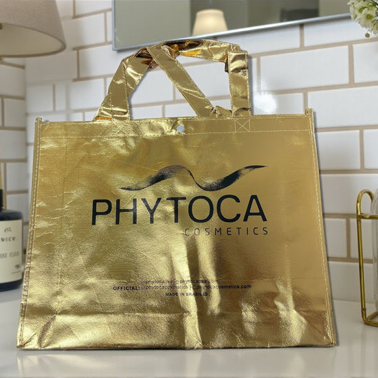 Bolsa de mano dorada metalizada Phytoca USA con logo negro impreso, ideal para cosméticos y accesorios.