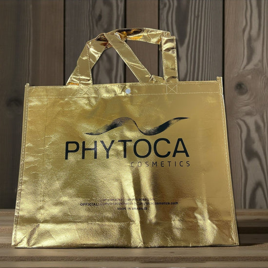 Bolsa de mano dorada Phytoca USA con acabado metálico y logo de Phytoca Cosmetics impreso en negro