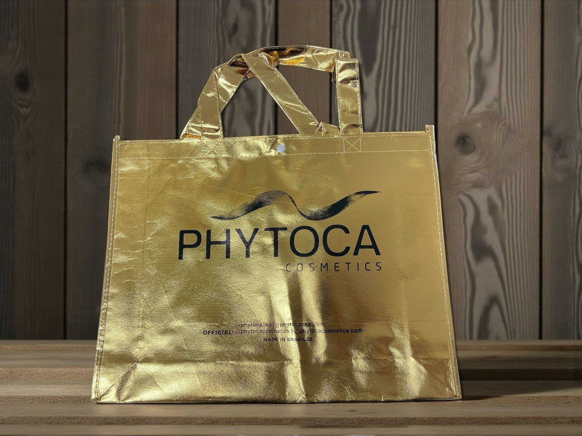 Bolsa de mano dorada Phytoca USA con acabado metálico y logo de Phytoca Cosmetics impreso en negro