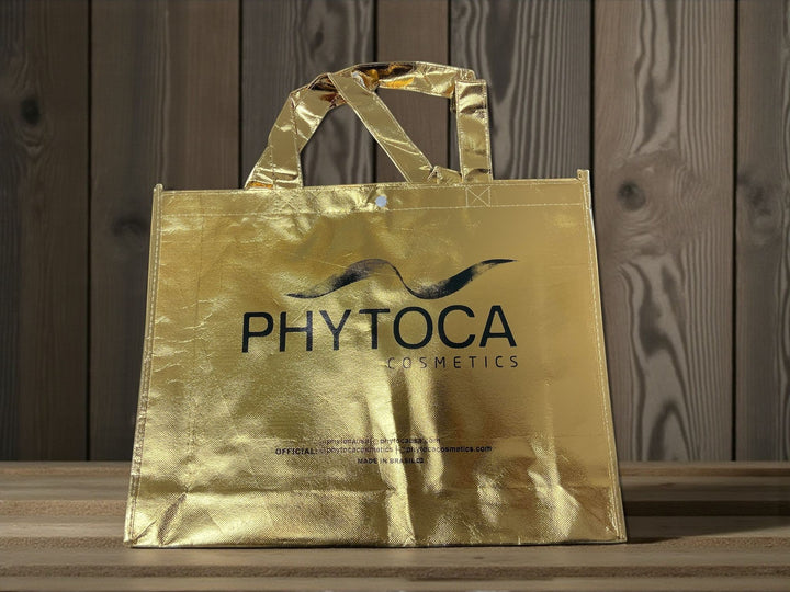 Bolsa de mano dorada Phytoca USA con acabado metálico y logo de Phytoca Cosmetics impreso en negro