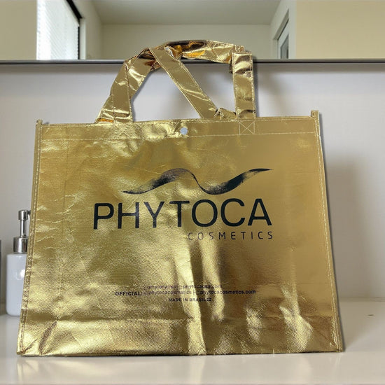 Bolso de mano Phytoca USA de color dorado brillante con el logotipo de la marca impreso en negro en el centro