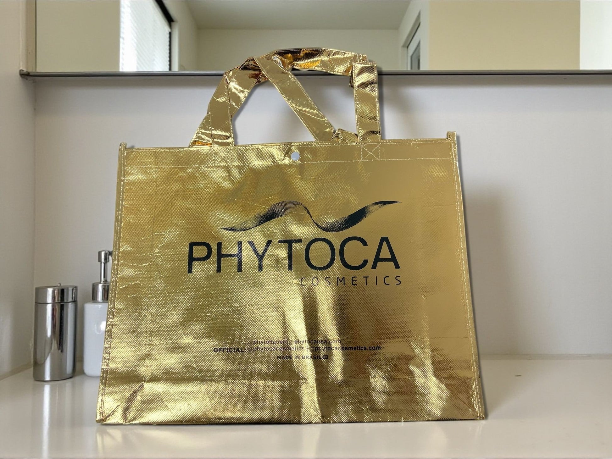 Bolso de mano Phytoca USA de color dorado brillante con el logotipo de la marca impreso en negro en el centro