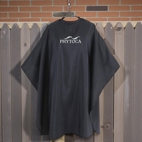 Capa de peluquería negra Phytoca USA con logo blanco, ideal para protección profesional en salones de belleza.