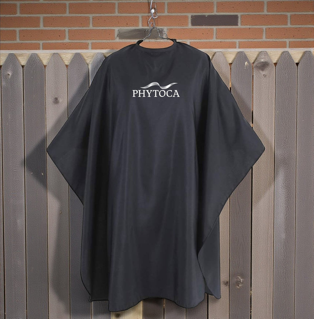 Capa de peluquería negra Phytoca USA con logo blanco, ideal para protección profesional en salones de belleza.