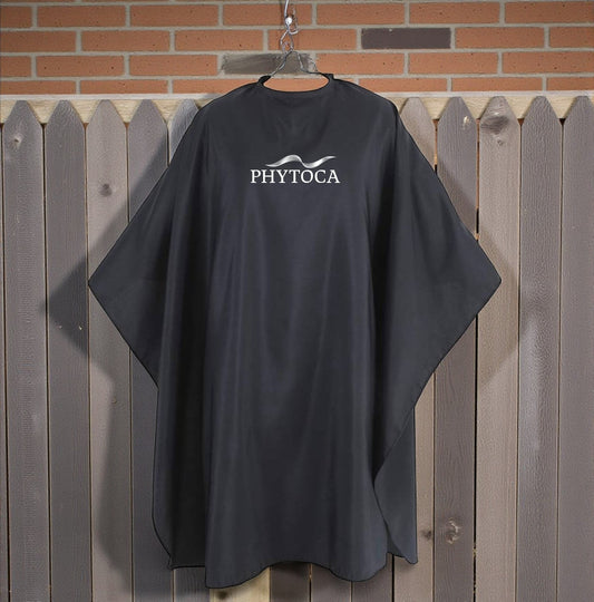 Capa de peluquería negra Phytoca USA con logo blanco, ideal para protección profesional en salones de belleza.