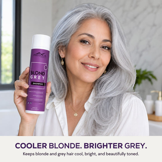 Mujer sonriente con cabello gris natural sosteniendo el champú Phytoca USA Blonde Grey para neutralizar tonos amarillos.
